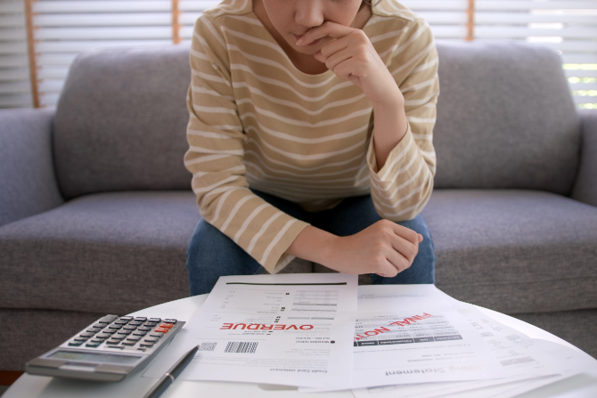Distressed woman calculating multiple bills and debts, contemplating whether to take a debt consolidation loan or not