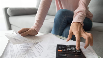 Stressed woman struggling with her multiple debts and loans, frantically counting the amount she owes using a calculator